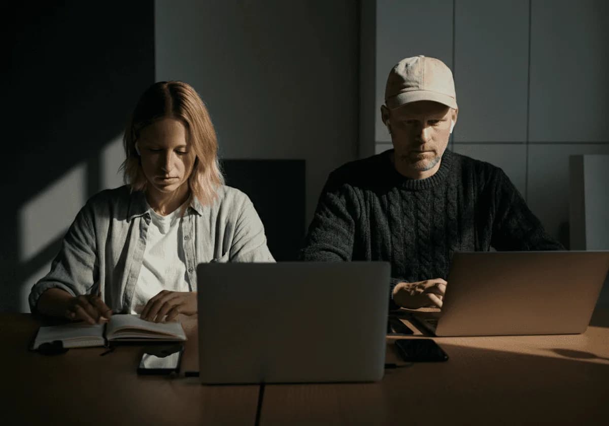 Dos personas trabajan con sus notebooks en una oficina en penumbra