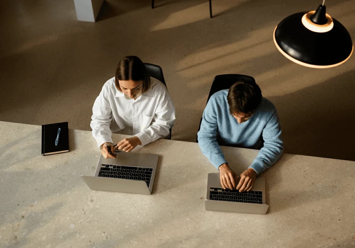 Dos personas trabajan con sus notebooks en un escritorio compartido