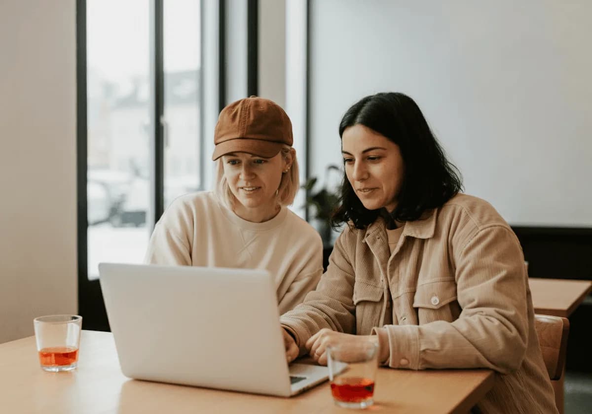 Dos personas miran juntas la pantalla de una notebook en la mesa de un café